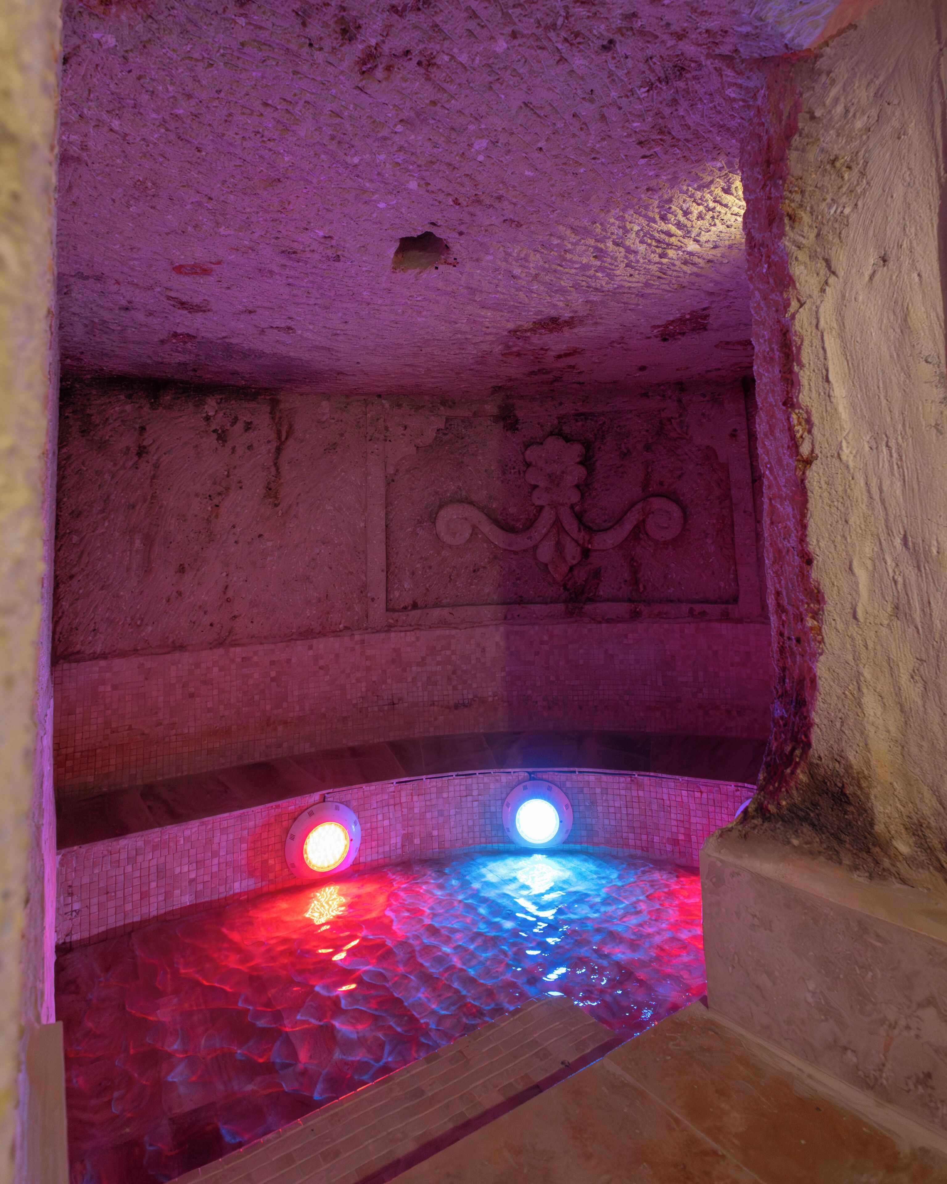 A stone interior with a tiled floor, a decorative wall, and two illuminated lights.