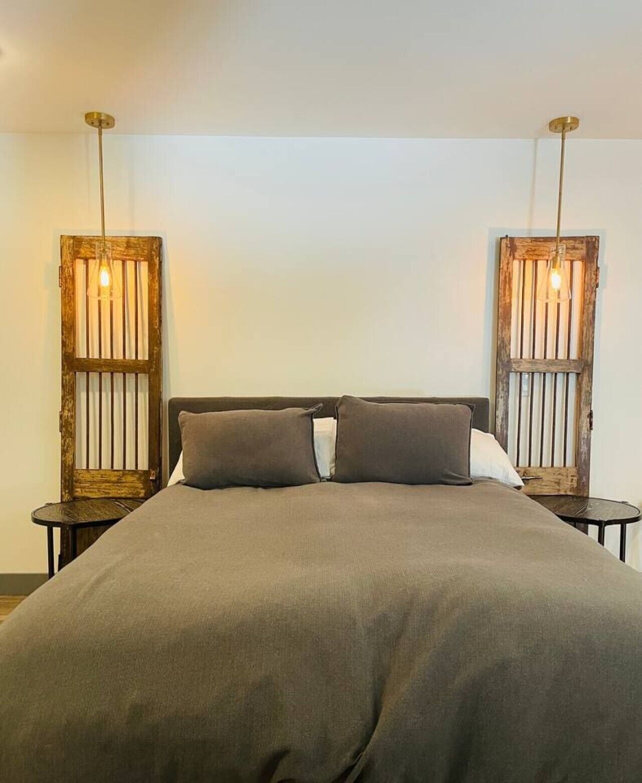 Un lit recouvert d’une couvre-lit de couleur sombre, deux tables de chevet avec des lampes et une tête de lit en bois avec des lattes verticales.