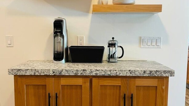 A kitchen with wooden cabinets, a granite countertop, a coffee maker, and glassware on shelves.