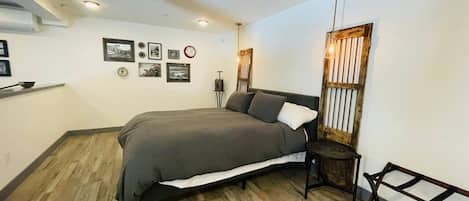 Un dormitorio con cama, piso de madera, un reloj de pared y cuadros enmarcados.