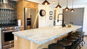 A modern kitchen with a granite countertop, stainless steel appliances, and a bar area with stools.