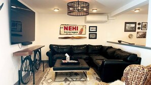 A living room with a black leather sofa, a coffee table, a television, a bicycle, and a sign for NEHI beverages.