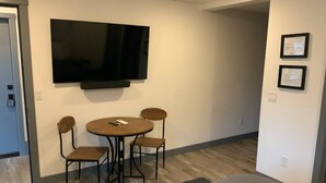 Una habitación con televisión de pantalla plana en la pared, una mesa redonda con cuatro sillas y una cama.
