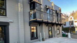 Un edificio de varios pisos con un balcón en el segundo nivel, una puerta de garaje y vista a la calle.