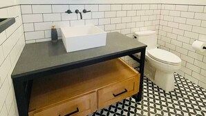 A bathroom with a black countertop, a white sink, a round mirror, and a toilet.