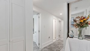 Un couloir avec des portes blanches, une table blanche ornée d’un vase de fleurs et un grand miroir.