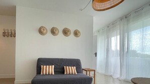 A modern living room with a grey sofa, striped cushions, a small wooden side table, and a black rug. - Côté Thalasso (Quiberon)