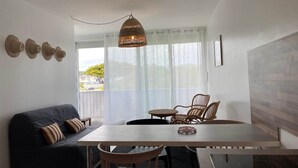 A modern living room with a sofa, dining table, chairs, and a hanging light fixture. - Côté Thalasso (Quiberon)