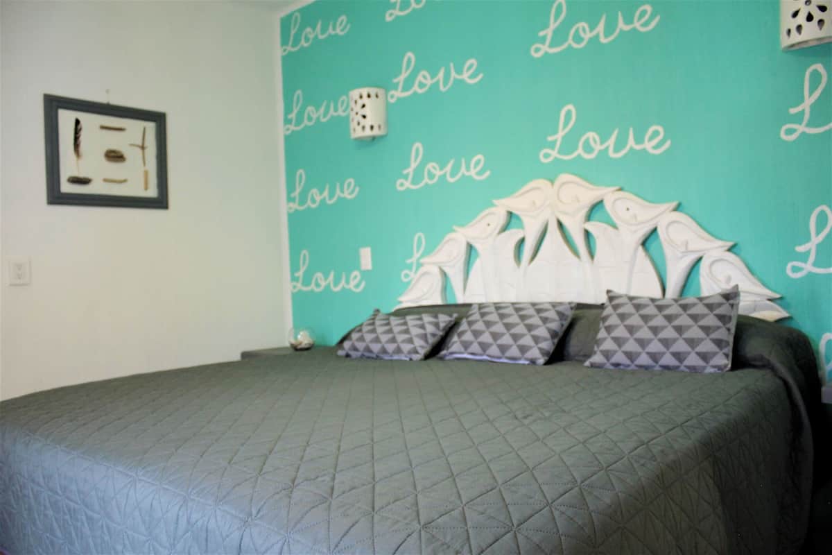 Een bed met een gewatteerde spreideken, een hoofdbord met decoratieve details, en een muur met de tekst 'Love' herhaald.