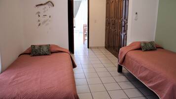 Two single beds with matching headboards and footboards, a tiled floor, and a door leading to an outdoor area.