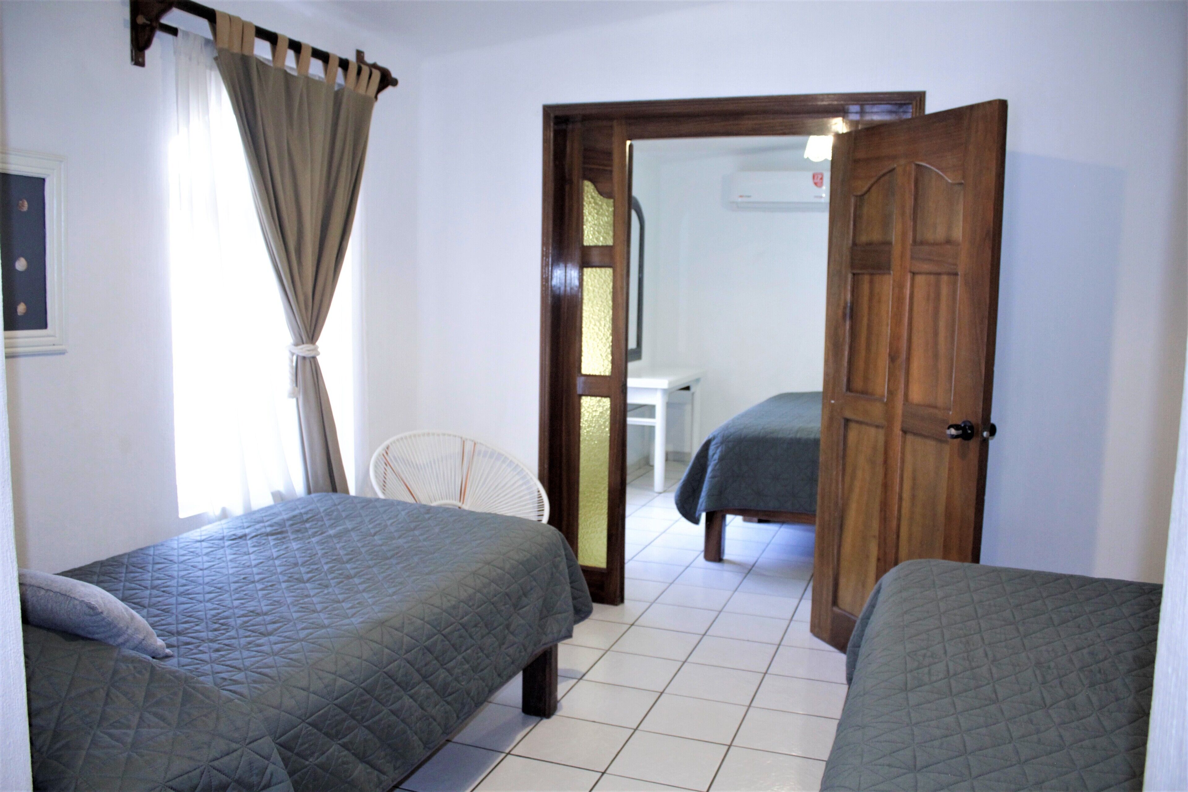 Une pièce avec deux lits, une chaise et une porte donnant sur une autre pièce.