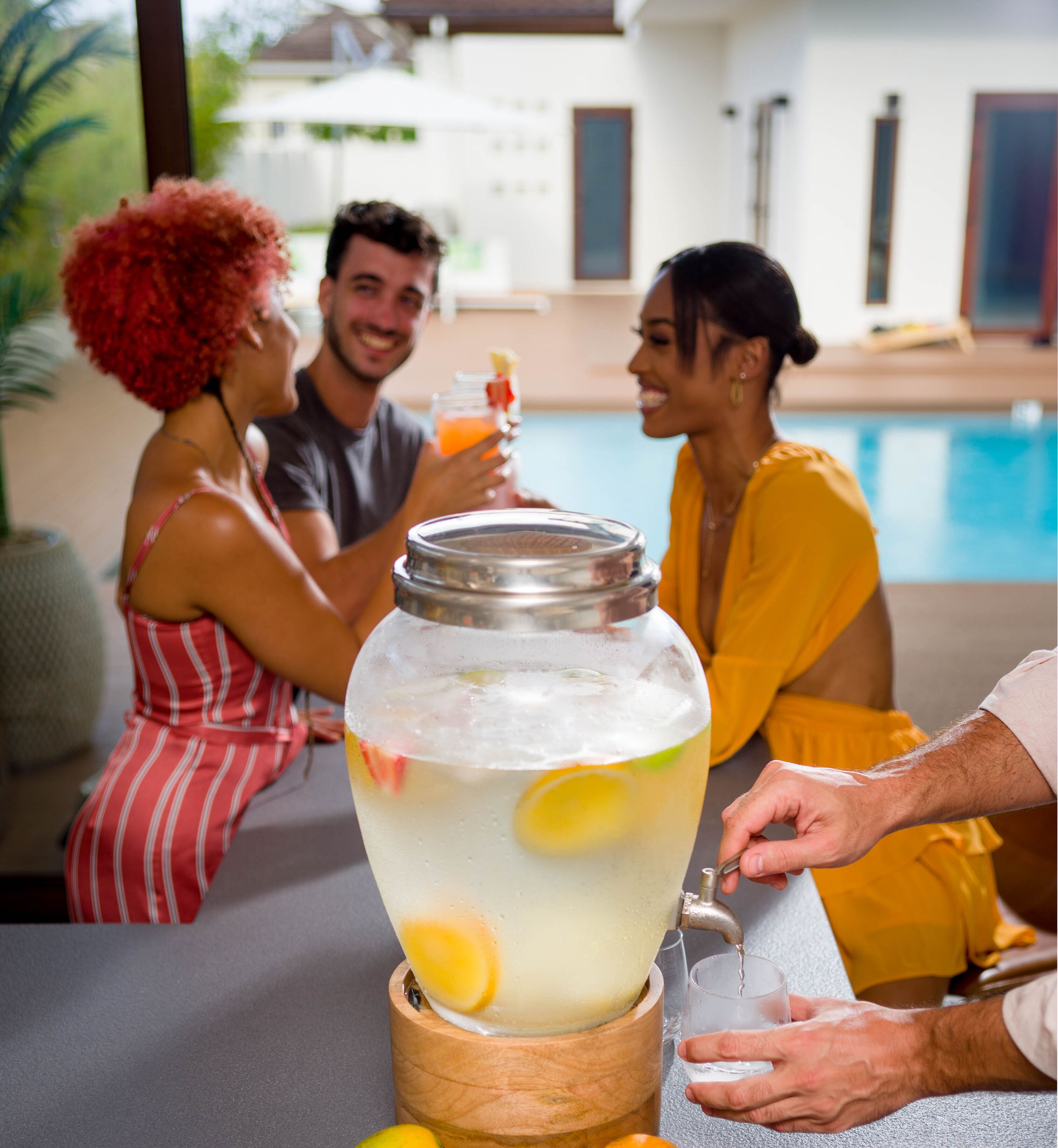 Un groupe de personnes est assis au bar, près de la piscine, et a devant lui une grande jarre de limonade.