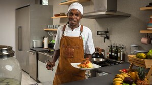 Una cocina moderna con electrodomésticos de acero inoxidable, estantes de madera con utensilios de cocina y una variedad de frutas y verduras sobre la encimera.