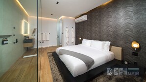 Una habitación de hotel moderna con una cama grande, suelo de madera, un espejo, un tocador con artículos de aseo y una pared con estampado de espiga.