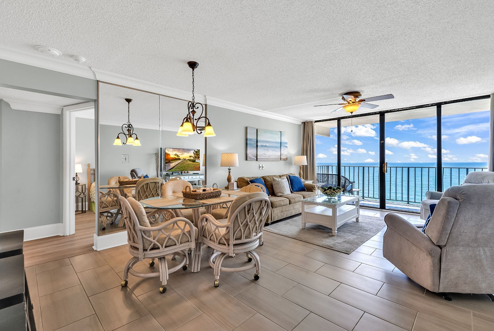A spacious living area with a dining table, cushioned chairs, a sofa, and a balcony with a view of the ocean.