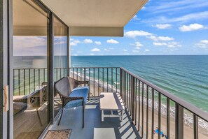 Ein Balkon mit Blick auf das Meer, Korbstühle, ein kleiner Tisch und eine Glastür.