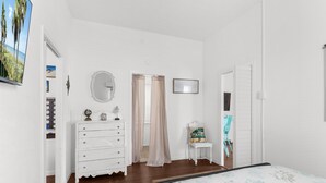 Une chambre à coucher comprenant un lit, une commode, un miroir, une fenêtre avec des rideaux et une petite table avec une chaise.