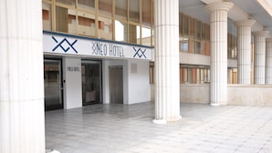 Entrada de un hotel con un letrero que dice "NEO HOTEL" y un diseño arquitectónico moderno que presenta columnas grandes y un piso de baldosas.