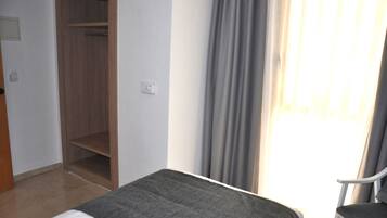 A hotel room with a bed, a chair, a wardrobe, and a window with curtains.