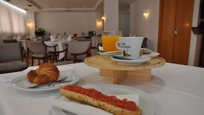 Un desayuno con cruasanes, una porción de pizza y un vaso de jugo de naranja sobre una mesa de madera.