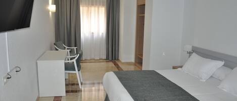 Habitación de hotel con cama, escritorio, silla, televisión y armario.