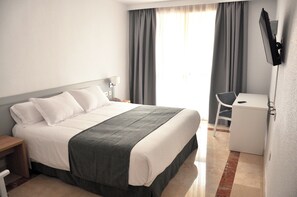 A hotel room with a bed, a desk, a chair, a TV mounted on the wall, and a window with curtains. - NEO HOTEL (Caravaca de la Cruz)