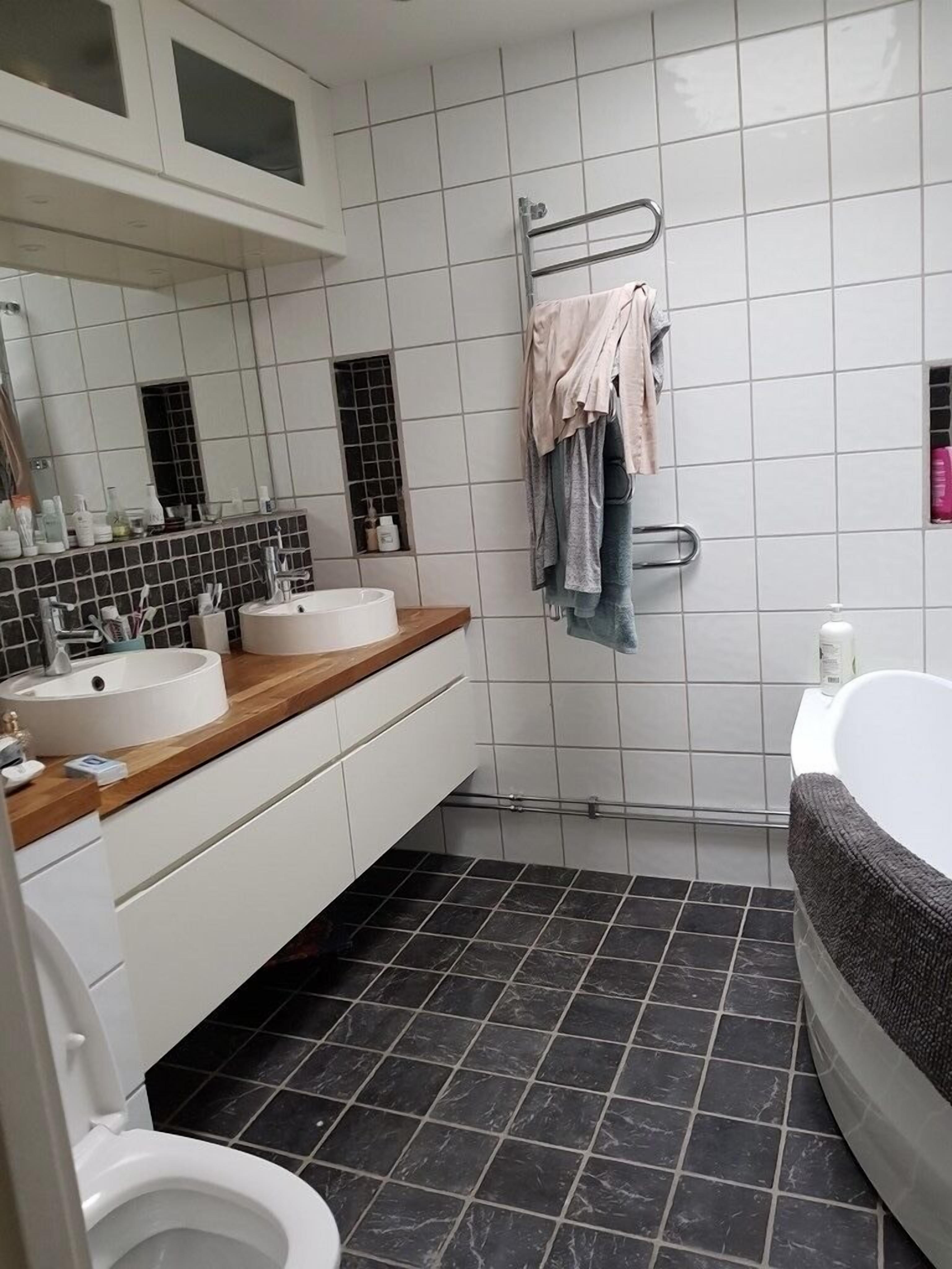 Une salle de bain moderne avec un lavabo blanc, un miroir et des toilettes. On y trouve également un espace douche avec un porte-serviettes et une baignoire.