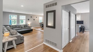 A modern living room with a grey sofa, a wooden coffee table, and a dining area with a white table and chairs. - Family Game House Near Kings Island (Mason)