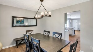 A dining area with a large table, six chairs, a chandelier, and a mirror on the wall. - Family Game House Near Kings Island (Mason)