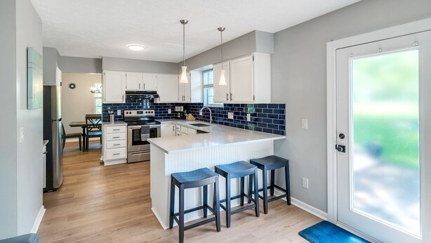 A modern kitchen with white cabinets, a central island with bar stools, and a large window providing natural light. - Family Game House Near Kings Island (Mason)
