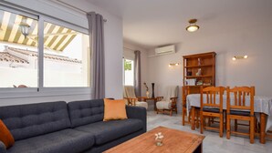 Een woonkamer met een bank, salontafel, houten stoelen, een boekenkast en een raam met gordijnen.