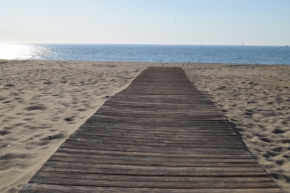 A wooden boardwalk leading to a sandy beach with a clear view of the ocean.