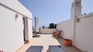 Een dakterras met twee loungestoelen, een tafel met stoelen, een potplant en uitzicht op zee.