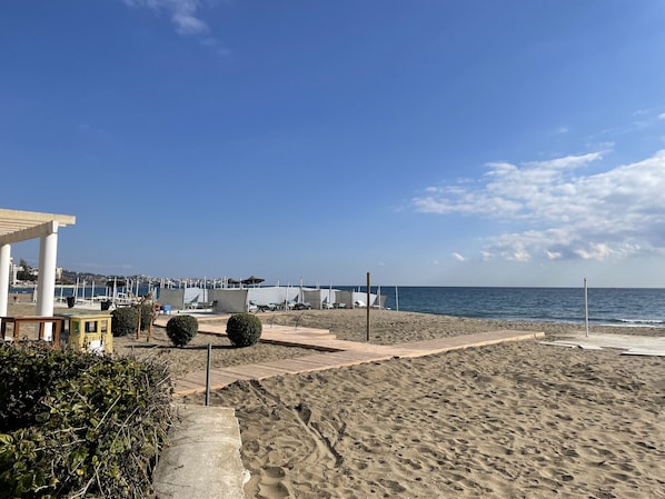 Une plage avec une promenade en bois menant à la mer, un espace de repos abrité et une vue sur l’océan.
