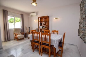Un coin repas avec une table dressée pour quatre personnes, des chaises en bois, une bibliothèque et une fenêtre avec des rideaux.