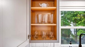 A kitchen cabinet with shelves holding glassware and a teapot. - Peaceful 1BR | Reading Nook | Near Portland (Westbrook)