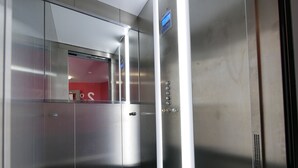 Interior de un ascensor con paredes metálicas, una pantalla digital y un panel de control con botones.