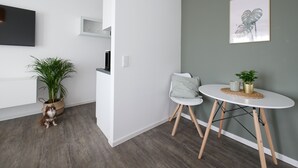 Una habitación moderna con pared gris, televisor montado, una mesita con una planta y una silla blanca.