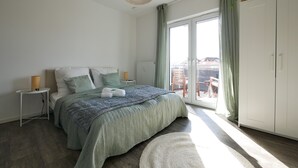 Un dormitorio moderno con una cama grande, una mesita de noche con lámpara, un armario y vistas al balcón exterior.