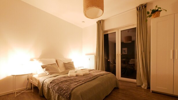 Un dormitorio con cama, mesitas de noche, lámpara colgante, puerta corrediza de vidrio y armario.