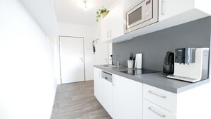 Una cocina moderna con armarios blancos, microondas, cafetera y un lavamanos.