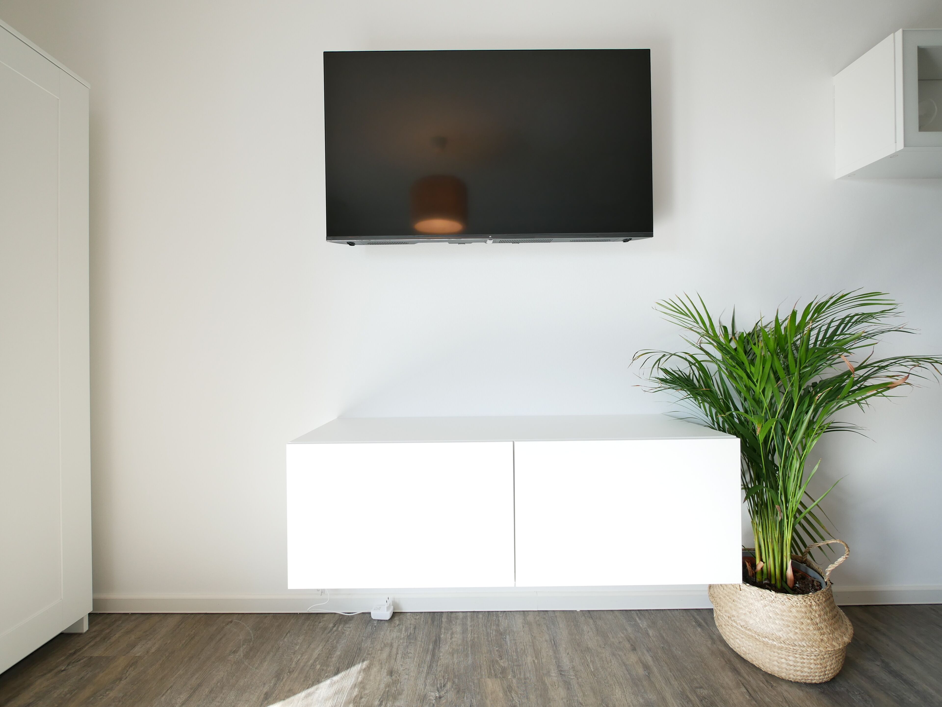 A modern living room with a mounted TV, a white cabinet, and a potted plant.