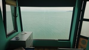 Eine kleine Holzhütte mit einem Einzelbett, einem Tisch mit einem Glas und einem Fenster mit Blick auf das Meer.