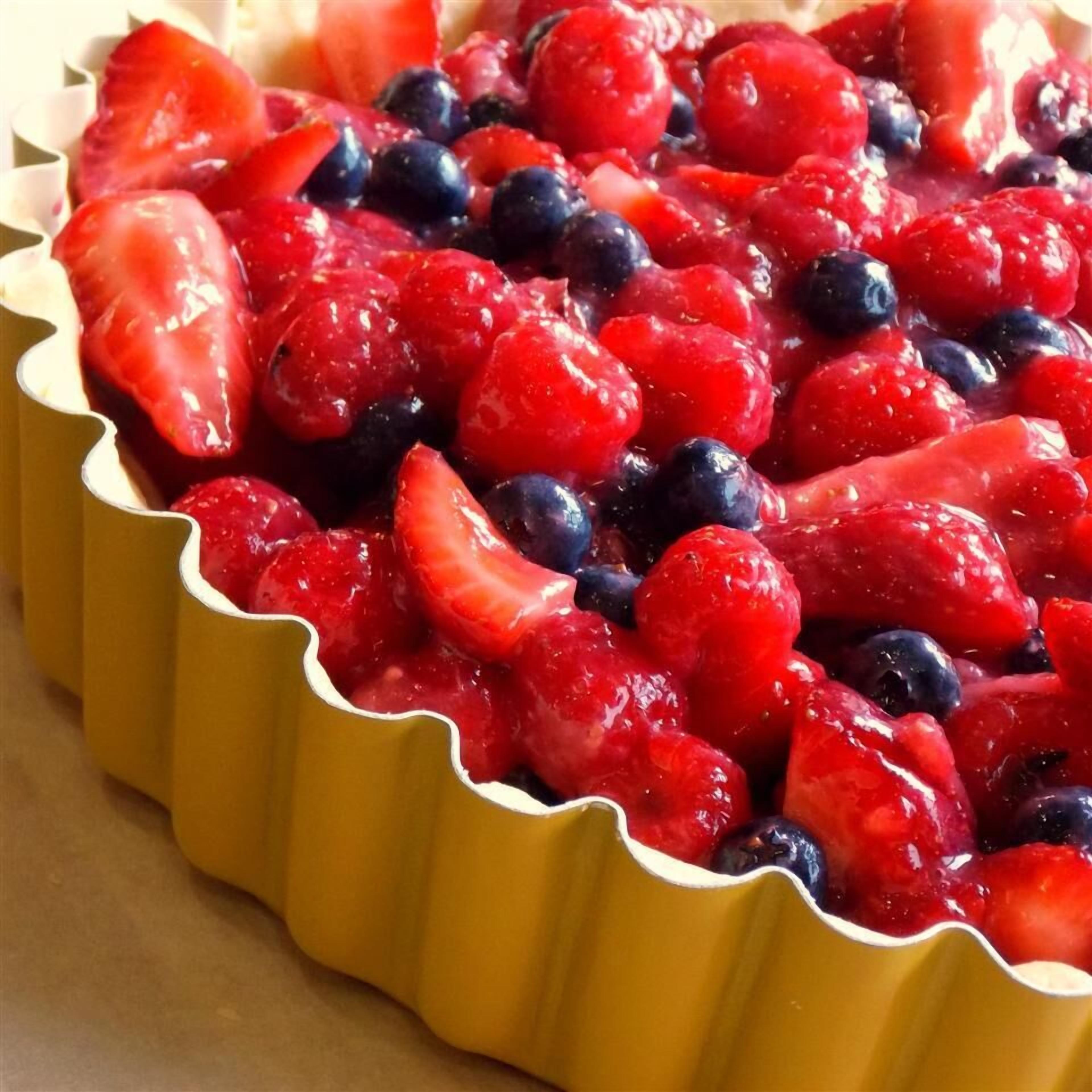 A dessert in a yellow tart shell with strawberries and blueberries.