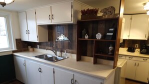 Une cuisine avec des armoires blanches, un pare-feu en bois et une étagère intégrée où sont exposés des objets décoratifs.