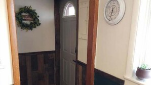 Un couloir avec une porte en bois, une horloge au mur et une petite plante en pot près de la fenêtre.