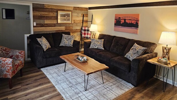 Un salon chaleureux avec deux canapés sombres, une table basse en bois et un tapis à motifs.