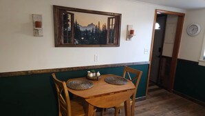Un coin repas avec une table et des chaises en bois, un tableau au-dessus de la table et une horloge au mur.