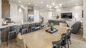 A spacious living area with a large dining table, dark chairs, a grey sofa, and a TV. - Waterpark overlook with patio, firepit, pickleball (Santa Clara)