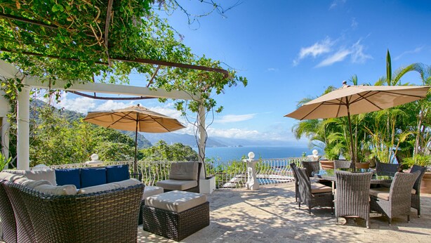 Un patio al aire libre con mobiliario de mimbre, sombrillas y vista al océano.